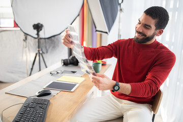 Cheerful middle eastern man photographer checking photographic flims at office