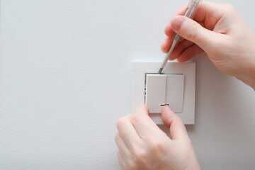 An electrician is replacing a wall switch. A DIY project concept. High voltage danger. Male...