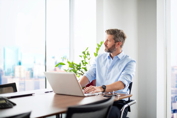 Fototapeta premium Confident professional man sitting at office desk and usin laptop for work