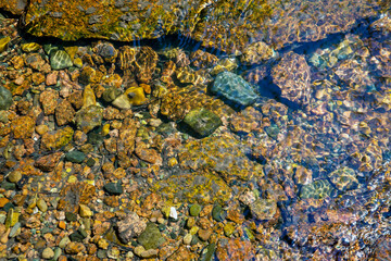 Small stones at the bottom of the river under a layer of clear water. Background from stones. Texture of water and stones.