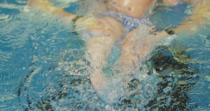Father holding little baby and helping to swim in swimming pool with clean blue water. Professional water therapy for kids . Swimming training from an early age . Parent having fun . Happy lifestyle
