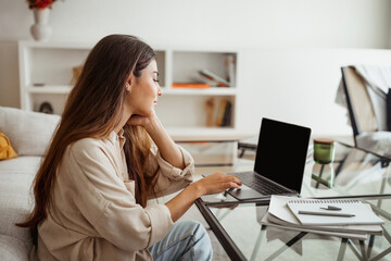 Smiling pretty millennial mixed race woman typing on laptop with empty screen in white living room