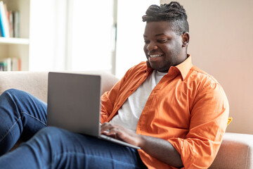 Cheerful black man digital nomad working from home, using laptop