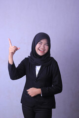 A woman in a black suit points her finger at the camera.