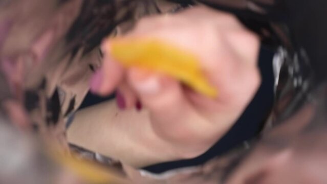 A young woman looks into a bag of crisps and eats them. View of a woman from a pack of chips.
