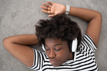 African American young woman listening to music on headphones while lying down on the floor. Black woman relaxing and resting.