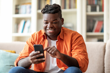 Positive cool overweight black guy using smartphone at home