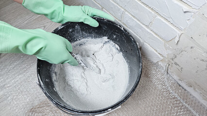 Gloved hands stir the putty, cement with a spatula in a bucket