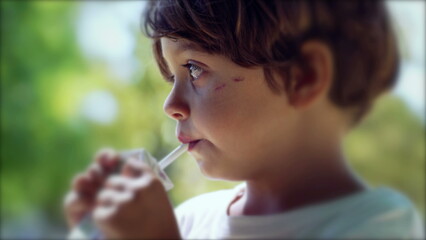 One thoughtful child drinking fruit juice with straw from carton box. Pensive kid snacking beverage