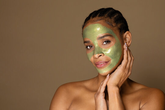 Portrait of african american middle aged woman with green peel-off mask on her face posing on brown background
