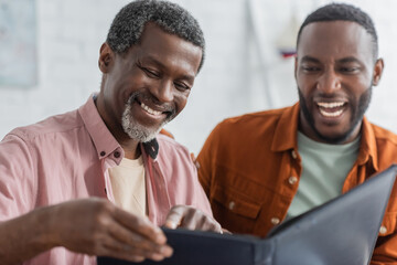 Obraz premium Carefree african american man pointing at blurred photo album near son at home.