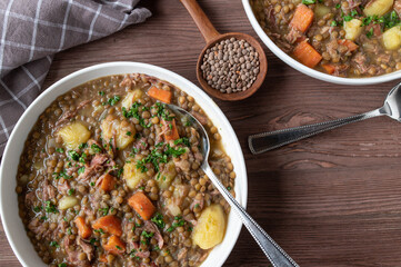 Lentil stew with potatoes, vegetables and smoked pork meat on a plate on wooden table from above