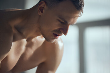Fototapeta na wymiar Close-up image of handsome young shirtless man with sweating face indoors. Fitness trainer after workout session. Concept of sportive lifestyle, body care, fitness, hobby, health, action and motion