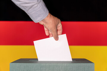 Man putting a ballot into a voting box against the background of the flag Germany