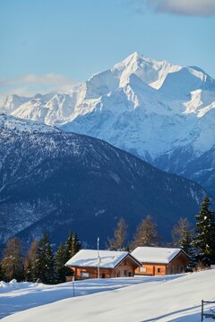 Fototapeta Vertical shot of the small huts nestled between the snowy mountains