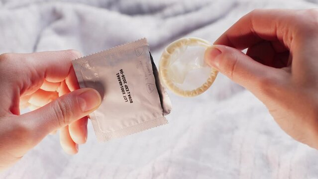 Man opening condom, close up, Hand holding a condom in package, close up on bedroom background
