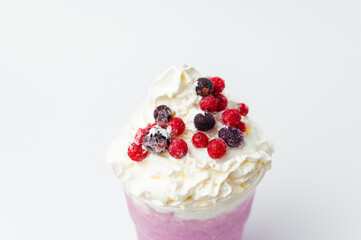 Close up shot of a tasty berry milkshake with whipped cream and currant on top.