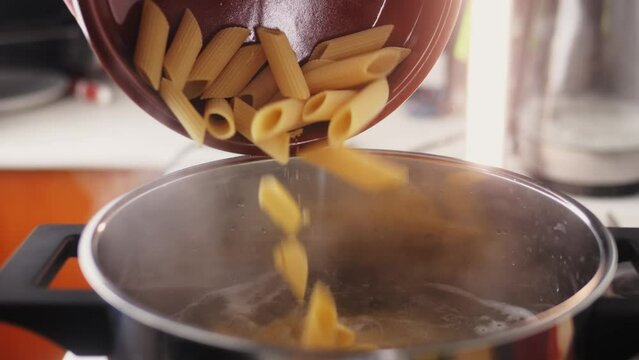 Male chef adding penne pasta into boiling water in pot. 