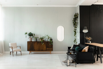 Interior with black leather sofa, pillows, wooden komodo, house flowers. Mid-century modern interior