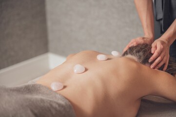 Obraz na płótnie Canvas Woman during spa massage procedure with white stones on her back