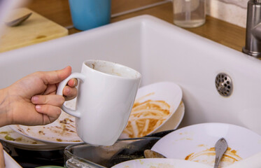 The child is in the kitchen. Small children's hands put the dirty mug in the sink. The concept of cleaning the house, helping parents, cleanliness and order
