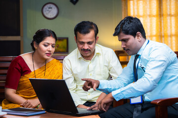 Banker showing insurance policy on laptop to couple at home - concept of financial advisor,...