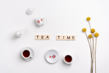 Cute tiny set of porcelain cups and saucers with yellow flowers on white background. Flat lay. TEA TIME made with tile letters