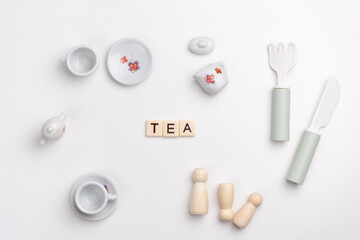 Flat lay of porcelain cups and saucers set, fork, knife and peg dolls on white background. Word TEA made with tile letters