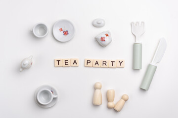 Flat lay of cute porcelain cups and saucers, fork, knife and peg dolls on white background. TEA PARTY written with tile letters