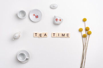 Flat lay of cute porcelain cups and saucers, fork, knife and peg dolls on white background. TEA TIME written with tile letters