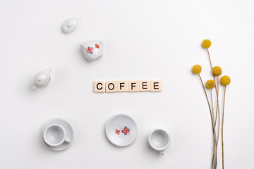 Cute tiny set of porcelain cups and saucers with yellow flowers on white background. Flat lay. COFFEE made with tile letters
