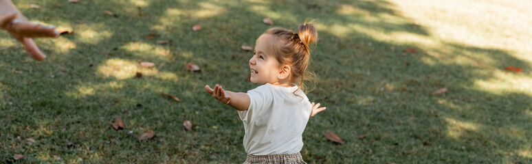 happy toddler girl standing with outstretched hands while playing in park, banner.