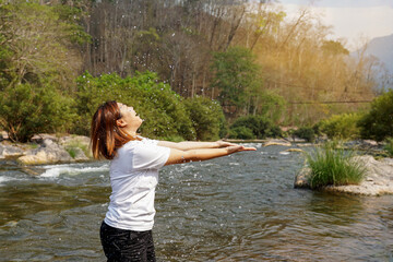 Asian woman walking in the stream, splashing water. She is happy, fresh and relaxed to experience nature, streams, mountains and fresh air at the national park.