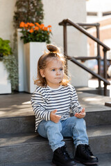 toddler girl in long sleeve shirt and jeans sitting on stairs near house.