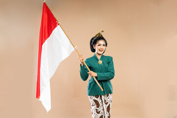 asian woman in green kebaya standing with smile while holding the indonesian flag with her both hands on isolated background
