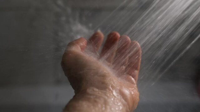 Water from the shower pours onto a man's hand in a stream, close-up