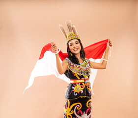 asian woman in traditional clothes of dayak tribe grab and waving the indonesian flag behind her body on isolated background