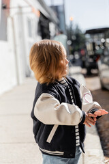 toddler girl in stylish bomber jacket walking on street in Miami.