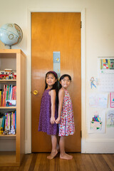 Two young asian girls standing next to growth marking ruler on door