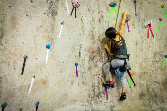 Young Asian Girl Reaching High In Indoor Rock Climbing Facility