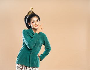 smiling asian woman in green kebaya looking and pointing on her left side while put her hand on her waist on isolated bacground