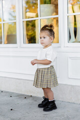 Obraz premium full length of toddler girl in skirt and white t-shirt standing near house.