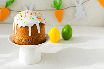 Traditional Ukrainian cake on a stand with candles in the shape of eggs on a white tablecloth. The concept of festive Easter baking. Selective focus. Horizontal orientation. Copy space.