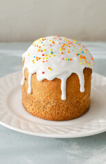Traditional Ukrainian kulich on a white plate on a gray background. The concept of festive Easter baking. Selective focus. Vertical orientation.