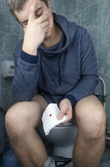 Hemorrhoid concept. A man sits on the toilet and holds white toilet paper in his hands. There is a...
