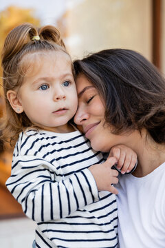 portrait of caring mother hugging toddler girl in striped long sleeve shirt.