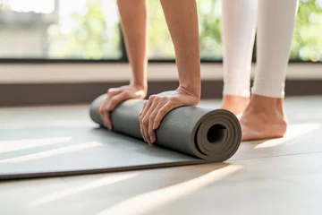 Foto op Plexiglas Fitness woman folding exercise mat before working out in yoga studio. rolling Yoga mat  after  training healthy lifestyle. © Charlie's
