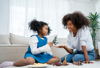 Overjoyed cute little girl baby child play rubber dinosaur with happy loving young mom, smiling african American mother and small kid.