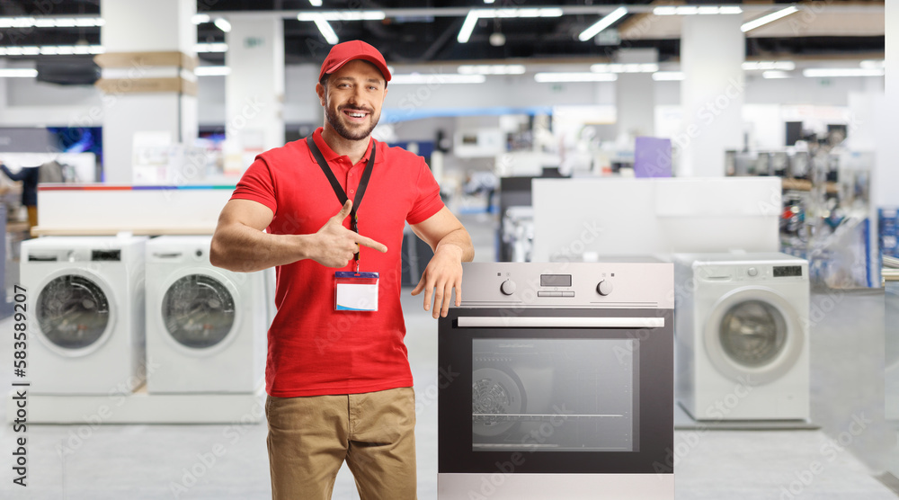 Wall mural Salesman with electrical appliances smiling and pointing at an oven in a store