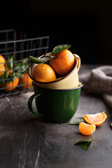 Ripe juicy clementines or tangerines with water drops in vintage mugs on dark concrete background. Side view, close up